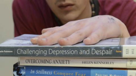 young man holding stack of books about mental illness