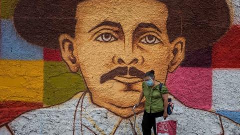 A woman walks by a mural of Jose Gregorio Hernandez, in Caracas