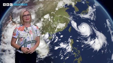 Sarah Keith-Lucas in front of a satellite weather map of Asia, showing Typhoon Khanun