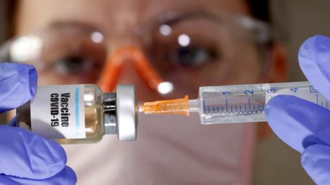 A nurse posing with a bottle marked Covid-19 vaccine