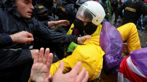 Police in black grab two protesters in yellow raincoats