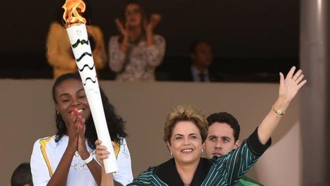 Brazilian volleyball player Fabiana Claudino (L) applauds as Brazilian President Dilma Rousseff holds the Olympic torch at Planalto Palace in Brasilia following the flame's arrival in the country on May 3, 2016