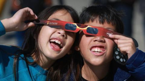 Miriam Toy (L) and Oliver Toy share a pair of eclipse glasses that NASA was handing out as they await the eclipse