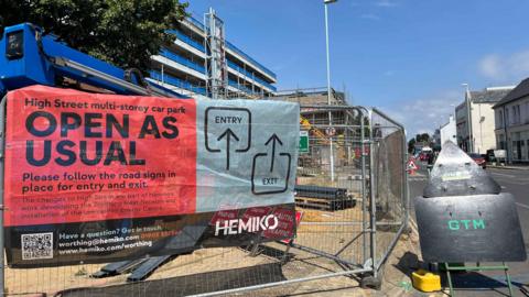 The Hemiko building site in the centre of Worthing. there is temporary fencing and excavators behind the fence. The brick plant can be seen being built next to a multistorey car park