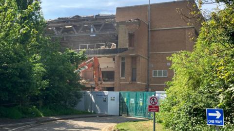 Regional Pool building with a collapsed roof and frontage and an orange digger in front of it 