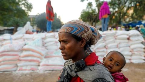 A woman carries an infant as she queues in line for food, at the Tsehaye primary school, in Shire, Tigray region, Ethiopia