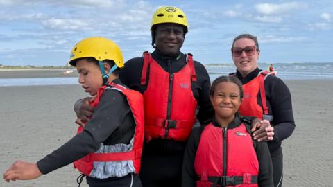Family of four wearing black wetsuits and red life jackets.