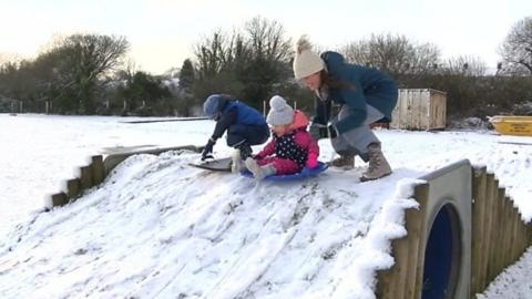 Mum pushing children down a hill on sleds