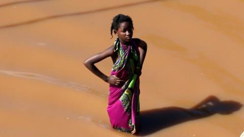 Girl looking at man carrying luggage over his head near Beira, Mozambique, on 22 March 2019