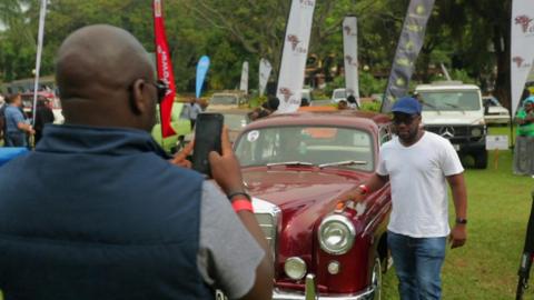 A man being photographed by a vintage car in Uganda