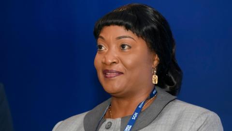 Jewel Howard-Taylor  wears a blue lanyard and grey jacket, gold earring at an economic forum in Poland, 2021. She has shiny black hair.
