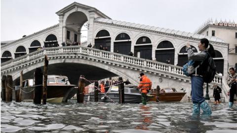 A tourist takes a photo from the flooded embankment by the Rialto bridge in Venice, 13 November 2019