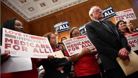Bernie Sanders stands with supporters of Medicare for All holding signs