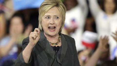 Hillary Clinton at a rally, over a podium labelled "stronger together"