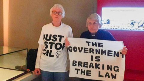 Reverend Sue Parfitt and Judy Bruce hold a sign which reads 'The Government is breaking the law'