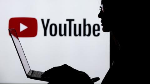 A silhouette of a woman with a laptop is seen in front of the logo of Youtube application in Ankara, Turkey on July 18, 2018