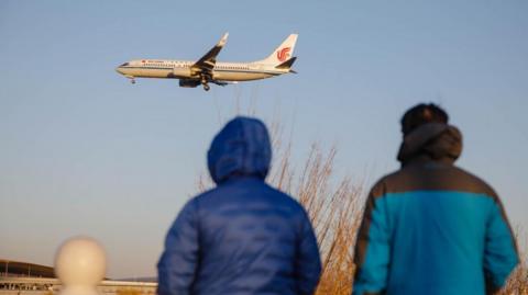 People watch a passenger plane landing at Beijing International Airport
