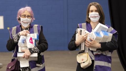 Two women in face masks carry hand sanitiser and other Covid cleaning products