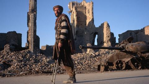 A man who lost his leg to a land mine walks past bomb-destroyed buildings