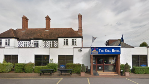 Image of the outside of the Bell Hotel in Epping Forest. The building is white with a blue sign on the door with yellow writing