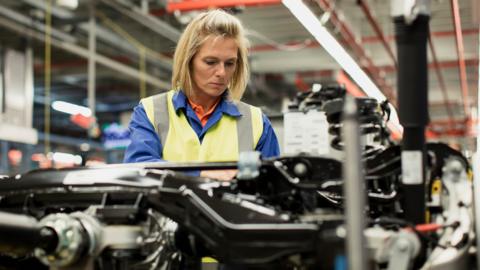 Female production line worker checking a car chassis