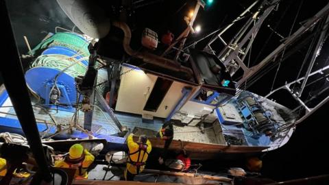 Looking down on fishing boat held next to the lifeboat by two RNLI men and a fisherman