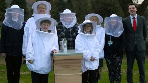 Staff and pupils standing next to a bee hive wearing protective equipment