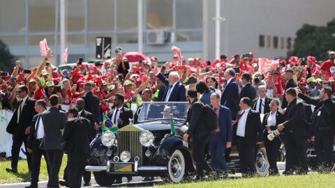 Lula waves at crowds from an open-topped car in Brazil.