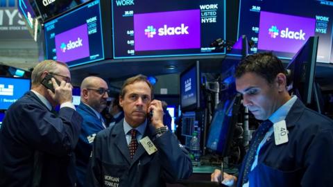 Traders gather around a post as they wait for shares of Slack to start trading