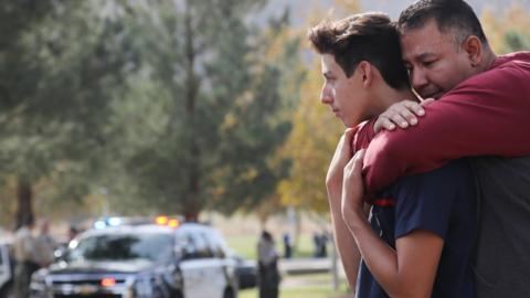 A father hugs his son after reuniting at a park near Saugus High School