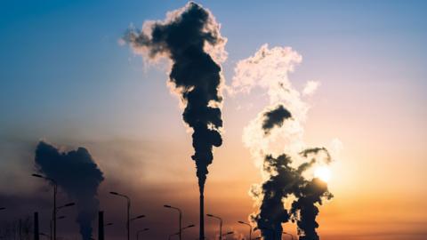 chimneys billowing smoke in front of a setting sun