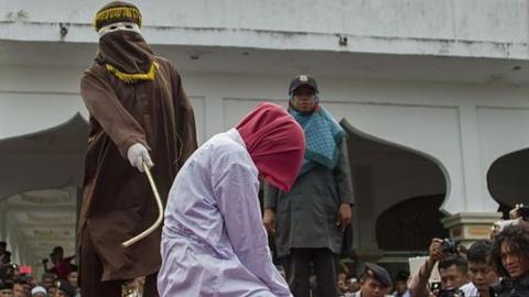 An Acehnese woman is lashed by a hooded local government officer during a public caning at a square in Aceh province, on June 12, 2015.