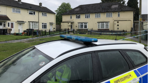 A police car with a grassy area behind it, surrounded by police tape