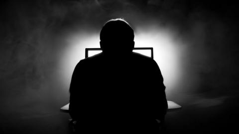 silhouette of man sat in front of computer