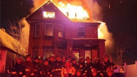 Fire crews posing for photo outside burning building