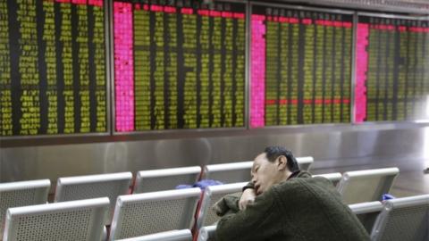 An investor takes a nap in front of an electronic board showing stock information at a brokerage house in Beijing