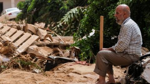 A man sits on a damaged car, after a powerful storm and heavy rainfall hit Libya, in Derna, Libya.