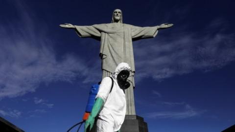 A worker wearing protective clothing stands in front of the Christ the Redeemer statue in Brazil