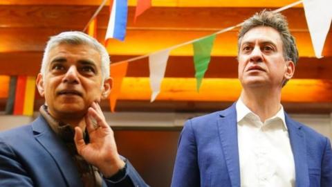 Sadiq Khan and Ed Miliband listening to someone as they visit a school in north London
