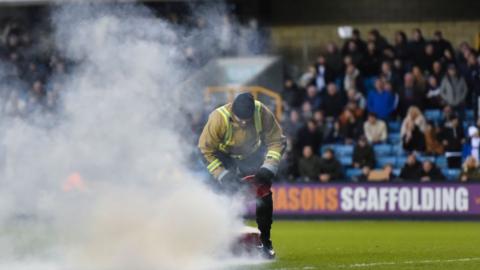 Three smokebombs were thrown onto the pitch at Millwall's New Den on Saturday, apparently from protesting West Brom fans