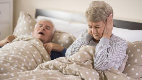 Older woman covering her ears in bed