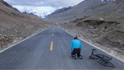 JJ Zhou kneels on the road next to his bike with Everest in the distance