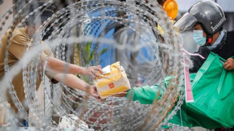 A resident receives packed food from a food delivery rider through the barbwire at the Segambut Dalam housing area which was placed under the enhanced movement control order (EMCO) due to surge in the number of COVID-19 daily cases recorded.