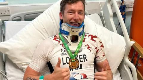 Matt Looker in a hospital bed wearing his bronze medal