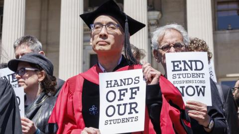 Professor in cap and gown holding sign