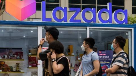 People walk past a pop-up store by asian e-commerce giant Lazada along Singapore's Orchard Road shopping district as it filled with crowds on Sunday, 12 December 2021.