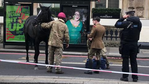 A horse being held by what appears to be an army officer, as police and other army staff look on
