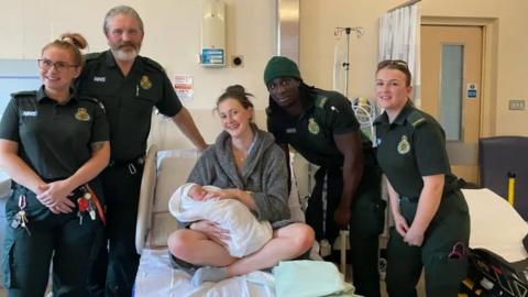 Phoebe with baby Lenny in bed with paramedics around her