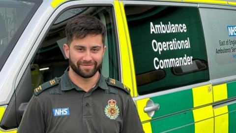 Man with short brown hair and beard standing in an ambulance uniform outside an ambulance