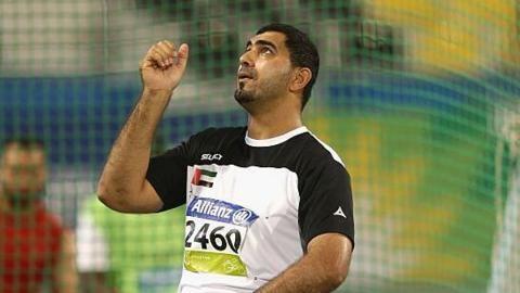 Abdullah Hayayei, wearing a sporting T-shirt with Allianz branding and competitor number 2460, stands in front of netting in a sporting arena and looks to the sky with a hand raised